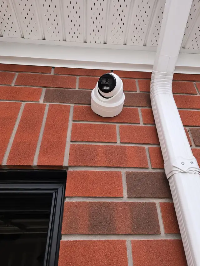 Security camera mounted tight to red brick beside a downspout in Erin Mills, Mississauga